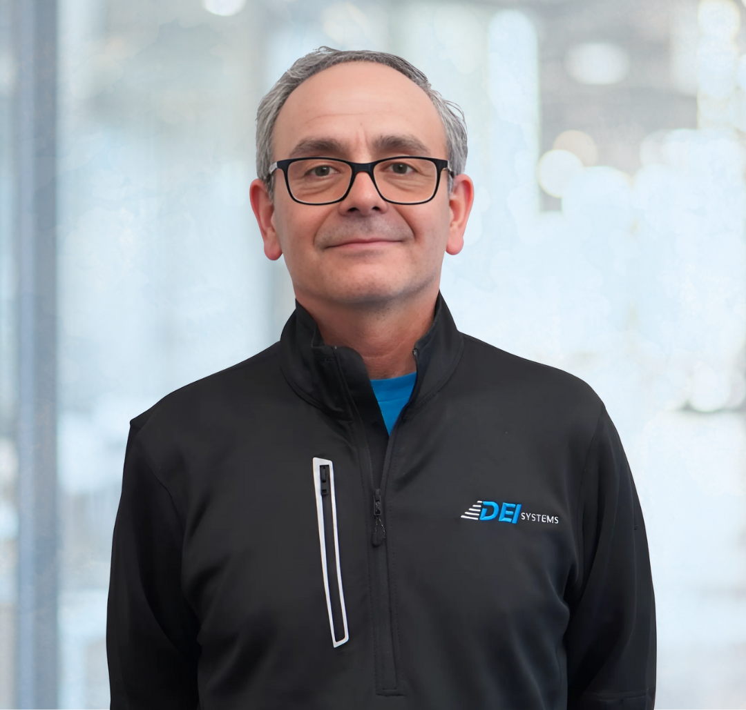 Luis Garcia A man wearing glasses and a black DE Systems jacket stands indoors in front of a blurred background.