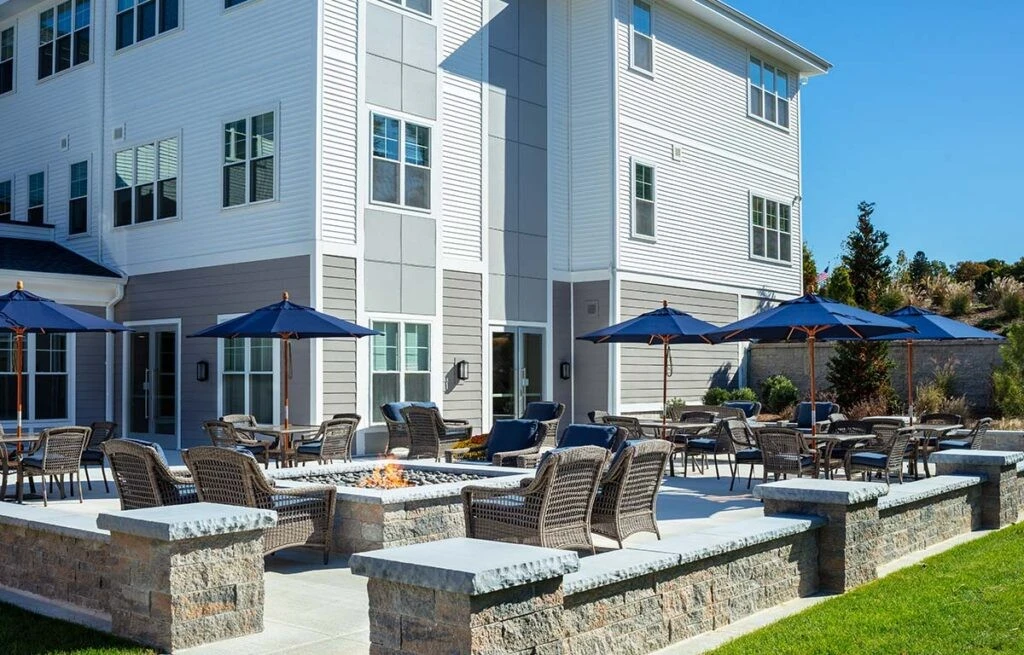 A patio with chairs and a fire pit in front of an apartment building.