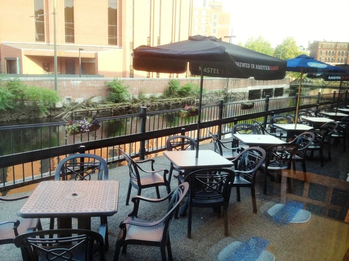 A group of tables and chairs on a balcony overlooking a river.
