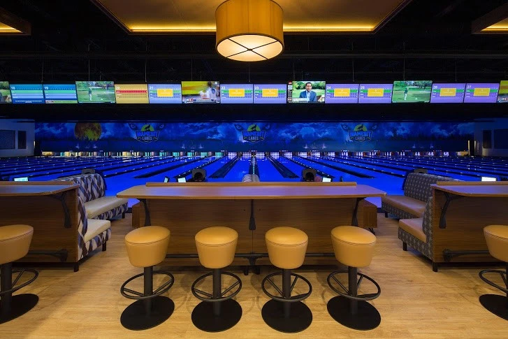 A bowling alley with a large screen and stools.