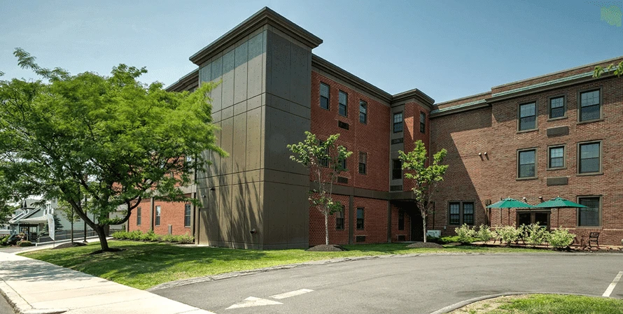 A red brick apartment building with trees and bushes.