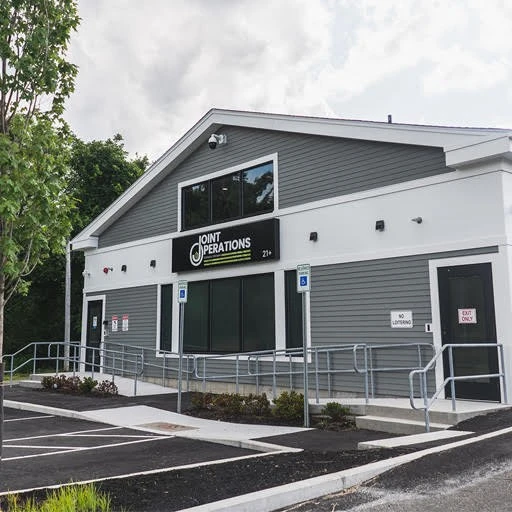 A gray building with a parking lot in front of it.